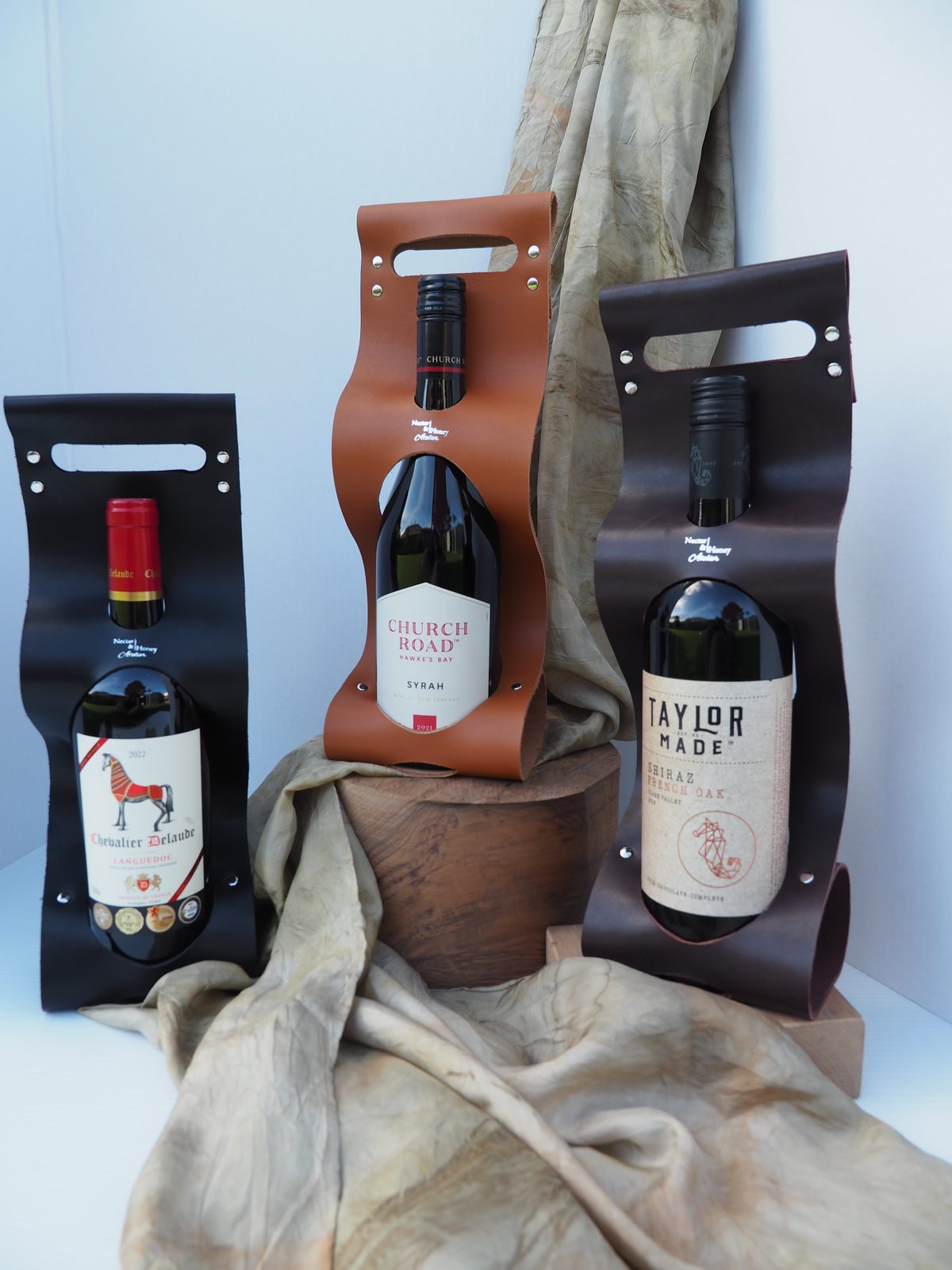 Tan, chocolate and black leather wine carriers together, each holding a bottle of wine